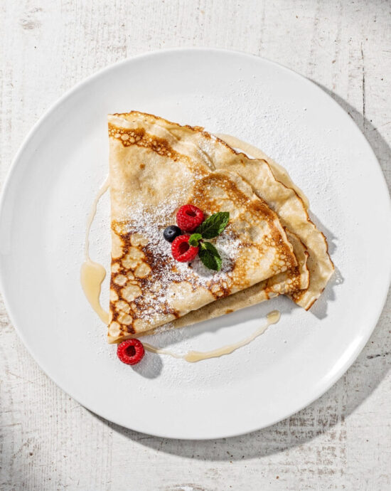 A stack of golden crepes with fresh berries and powdered sugar, showcasing the perfect results of this simple crepe recipe.