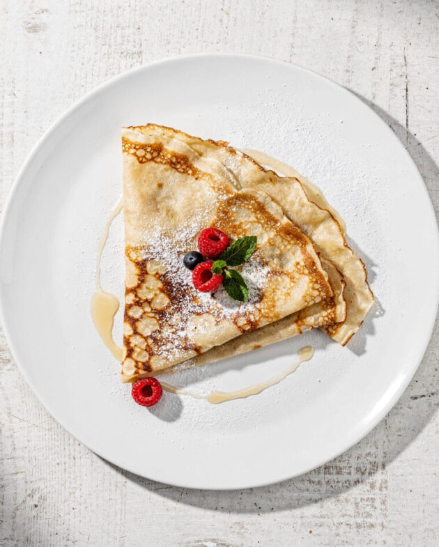 A stack of golden crepes with fresh berries and powdered sugar, showcasing the perfect results of this simple crepe recipe.
