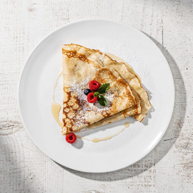 A stack of golden crepes with fresh berries and powdered sugar, showcasing the perfect results of this simple crepe recipe.