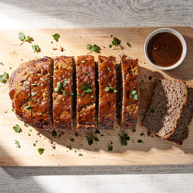 A perfectly cooked meatloaf recipe on a rustic cutting board, drizzled with glaze and ready to be sliced.