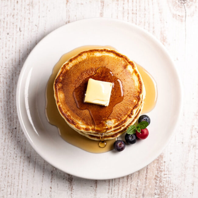 A tall stack of golden brown pancakes from this classic pancake recipe, drizzled with maple syrup.