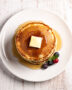 A tall stack of golden brown pancakes from this classic pancake recipe, drizzled with maple syrup.