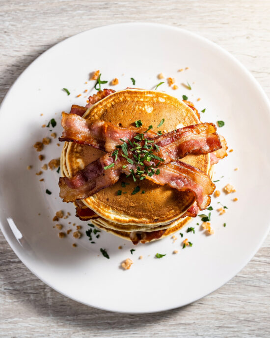 A stack of golden-brown bacon pancakes drizzled with maple syrup, ready for a perfect weekend breakfast.