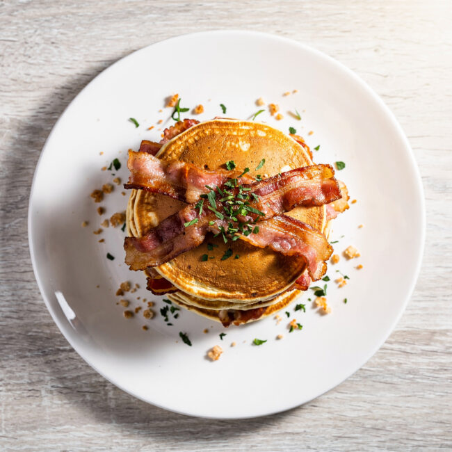 A stack of golden-brown bacon pancakes drizzled with maple syrup, ready for a perfect weekend breakfast.