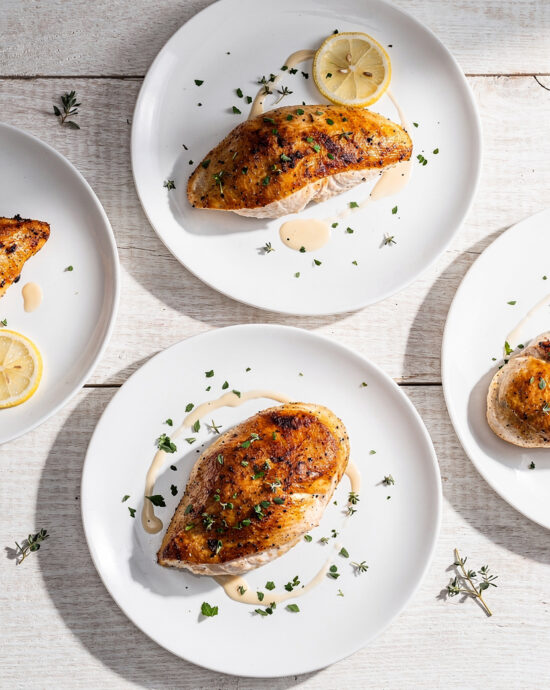 A top-down view of perfectly cooked baked chicken breast recipes on a light wooden table.