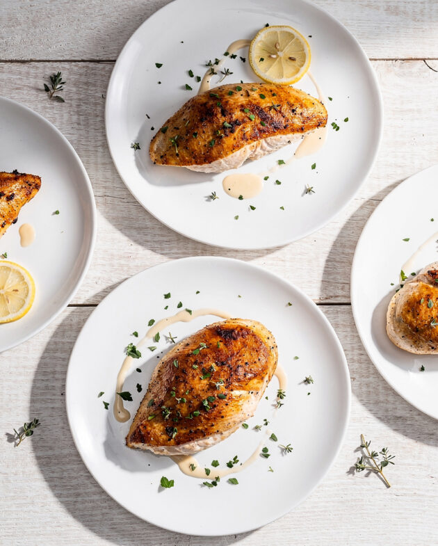 A top-down view of perfectly cooked baked chicken breast recipes on a light wooden table.