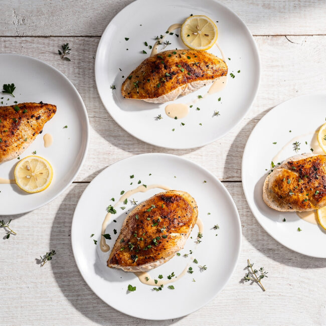 A top-down view of perfectly cooked baked chicken breast recipes on a light wooden table.
