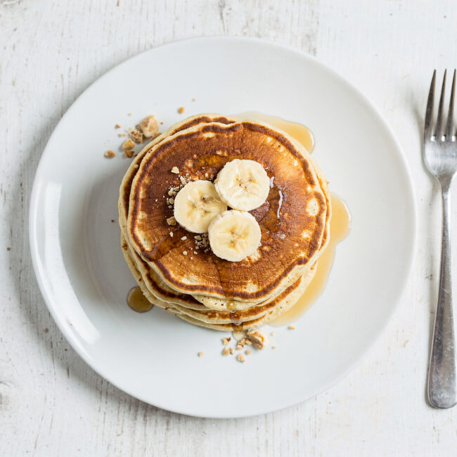 A stack of golden-brown banana pancake recipe drizzled with maple syrup, shot in soft morning light.