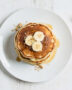 A stack of golden-brown banana pancake recipe drizzled with maple syrup, shot in soft morning light.