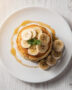 A tall stack of golden brown banana pancakes dripping with syrup, ready for a cozy breakfast.