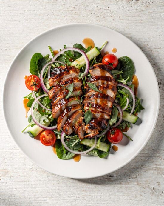 An overhead shot of a vibrant BBQ chicken salad, showcasing shredded smoky chicken, black beans, corn, crisp lettuce, and a creamy dressing drizzled on top.