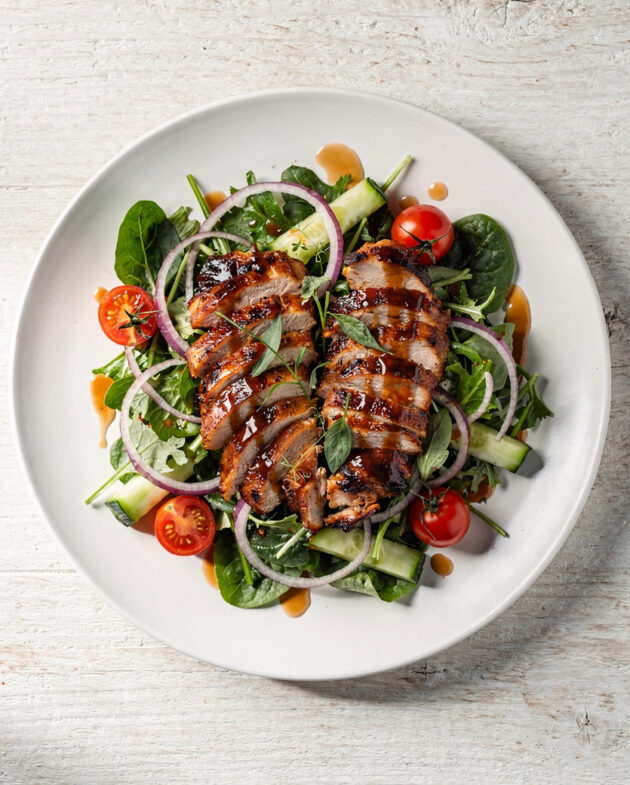 An overhead shot of a vibrant BBQ chicken salad, showcasing shredded smoky chicken, black beans, corn, crisp lettuce, and a creamy dressing drizzled on top.