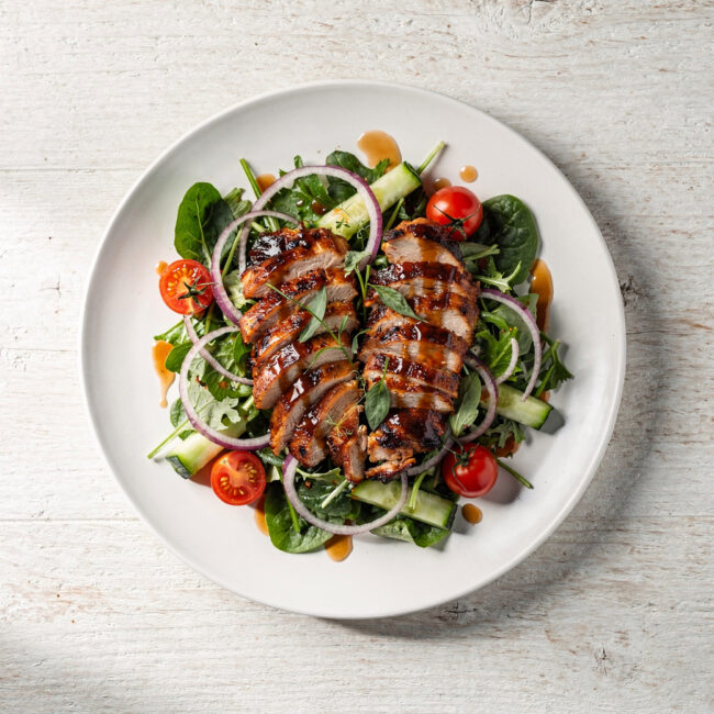 An overhead shot of a vibrant BBQ chicken salad, showcasing shredded smoky chicken, black beans, corn, crisp lettuce, and a creamy dressing drizzled on top.