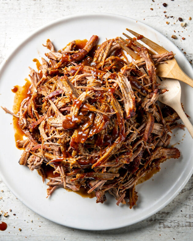 A close-up shot of succulent, glazed bbq pork in the oven, shredded and ready to serve on a wooden board.