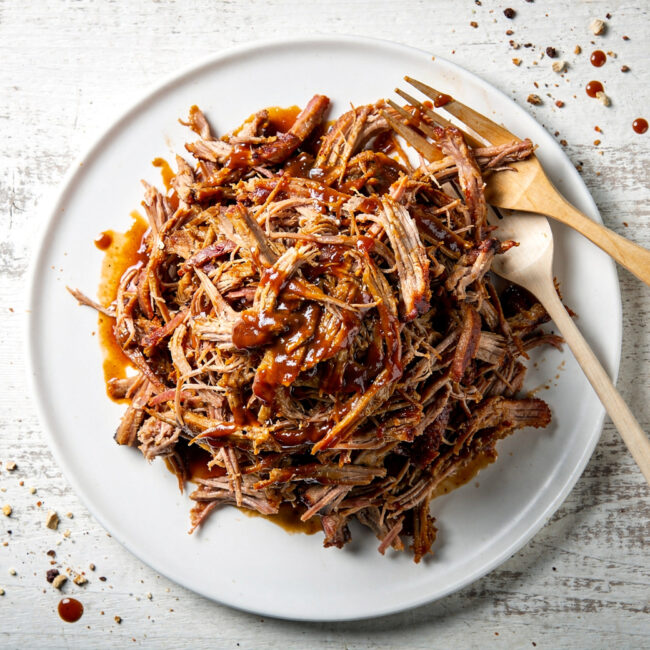 A close-up shot of succulent, glazed bbq pork in the oven, shredded and ready to serve on a wooden board.