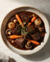 A steaming bowl of the finished beef bourguignon recipe, garnished with parsley, sits on a rustic wooden table.