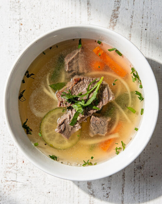 A rustic bowl of golden homemade beef broth for vegetable soup, garnished with fresh thyme.