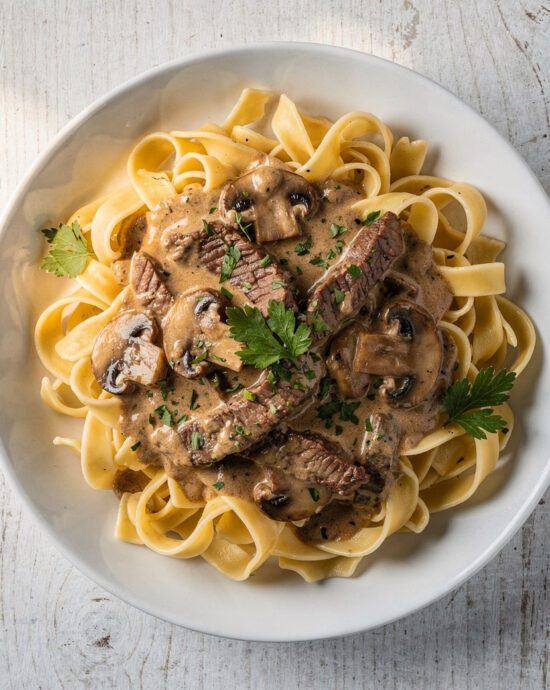 A top-down view of the finished beef stroganoff recipe, showcasing creamy sauce, tender beef, and herbs over egg noodles.