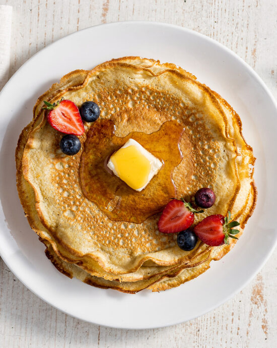 A stack of golden, delicate crepes from the best crepe recipe, drizzled with honey and berries.