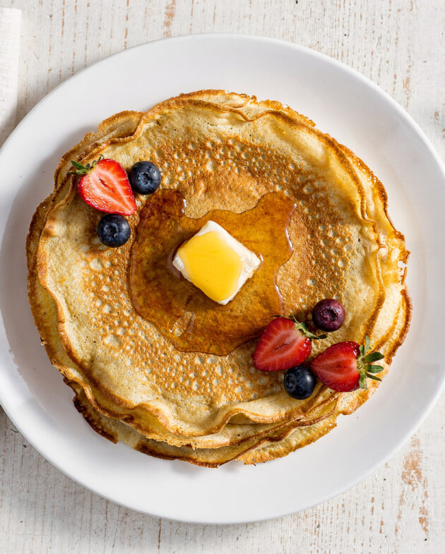 A stack of golden, delicate crepes from the best crepe recipe, drizzled with honey and berries.
