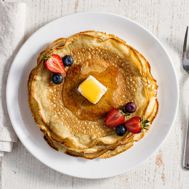 A stack of golden, delicate crepes from the best crepe recipe, drizzled with honey and berries.