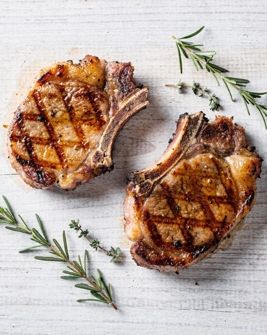 A perfectly grilled pork chop with a smoky crust rests on a wooden board, illustrating the best way to grill pork chops.