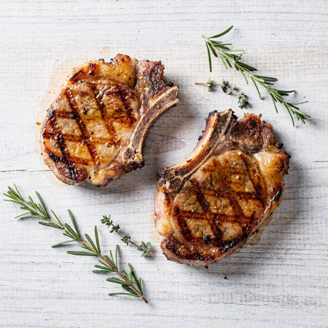A perfectly grilled pork chop with a smoky crust rests on a wooden board, illustrating the best way to grill pork chops.