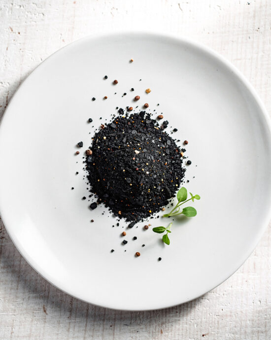 A jar of homemade black steak seasoning sits on a rustic wooden table next to a perfectly grilled steak.