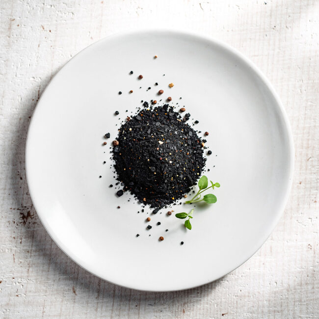 A jar of homemade black steak seasoning sits on a rustic wooden table next to a perfectly grilled steak.