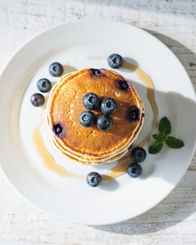 A stack of fluffy blueberry pancakes with maple syrup drizzled down the sides.