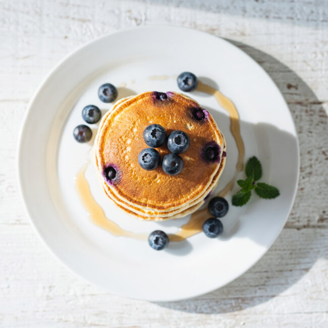 A stack of fluffy blueberry pancakes with maple syrup drizzled down the sides.