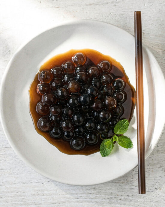 A close-up, inviting shot of freshly cooked boba tea tapioca pearls glistening in a simple syrup.