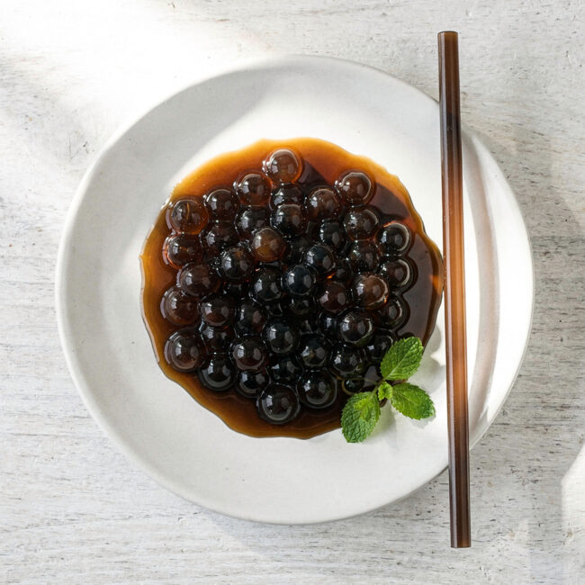 A close-up, inviting shot of freshly cooked boba tea tapioca pearls glistening in a simple syrup.