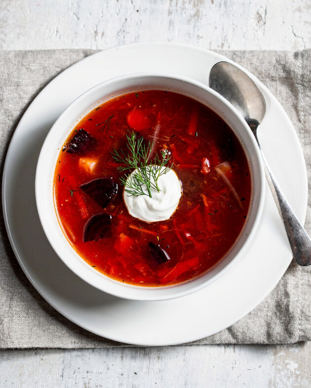 A steaming bowl of vibrant borscht soup garnished with fresh dill and a dollop of sour cream.