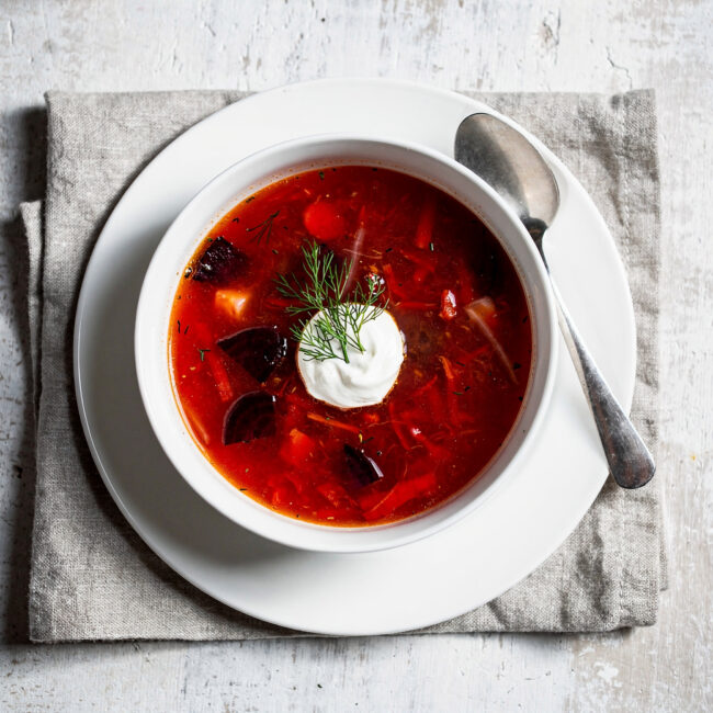 A steaming bowl of vibrant borscht soup garnished with fresh dill and a dollop of sour cream.