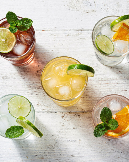 An overhead view of vibrant Brazilian cocktails in glass tumblers on a rustic wood table.