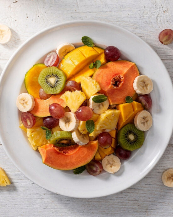 A vibrant, creamy bowl of brazilian fruit salad overflowing with mango, papaya, and bananas.