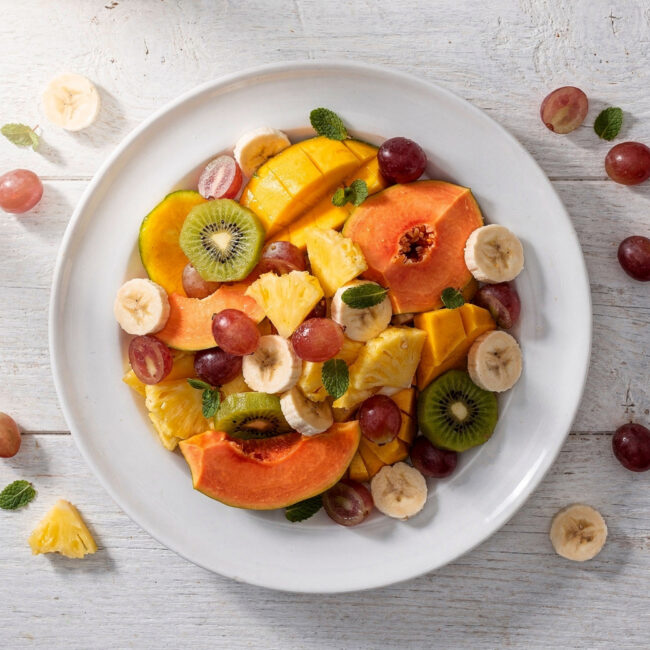 A vibrant, creamy bowl of brazilian fruit salad overflowing with mango, papaya, and bananas.