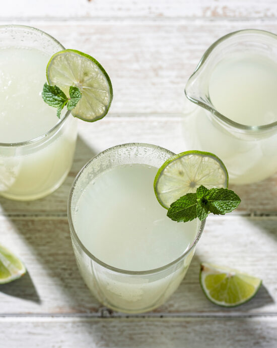 A frosty glass of creamy Brazilian limeade sits on a sun-drenched wooden table.