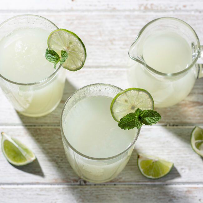 A frosty glass of creamy Brazilian limeade sits on a sun-drenched wooden table.