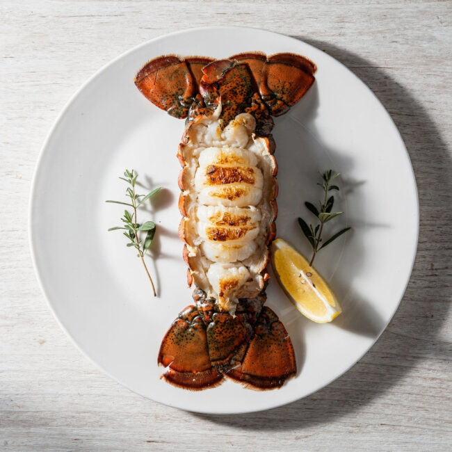 A perfectly grilled Brazilian lobster tail with creamy herb butter sauce on a wooden board.
