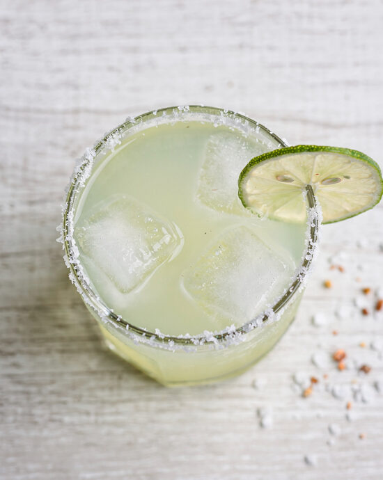 A frosty glass of Brazilian margarita with a salted rim, garnished with a lime wheel and a slice of fresh passion fruit.