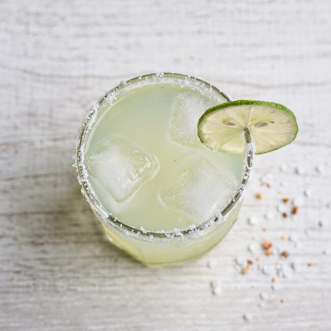 A frosty glass of Brazilian margarita with a salted rim, garnished with a lime wheel and a slice of fresh passion fruit.