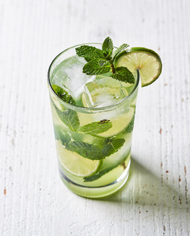 An inviting brazilian mojito in a highball glass, with fresh mint and citrus slices, on a rustic wooden table.