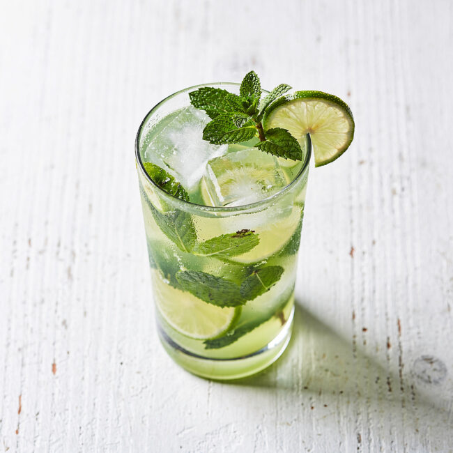 An inviting brazilian mojito in a highball glass, with fresh mint and citrus slices, on a rustic wooden table.