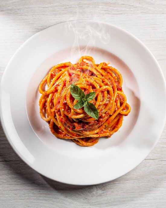 A vibrant bowl of Brazilian pasta topped with fresh herbs and ground peanuts on a rustic wood table.