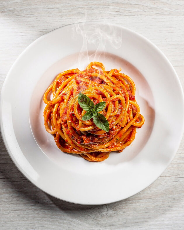A vibrant bowl of Brazilian pasta topped with fresh herbs and ground peanuts on a rustic wood table.