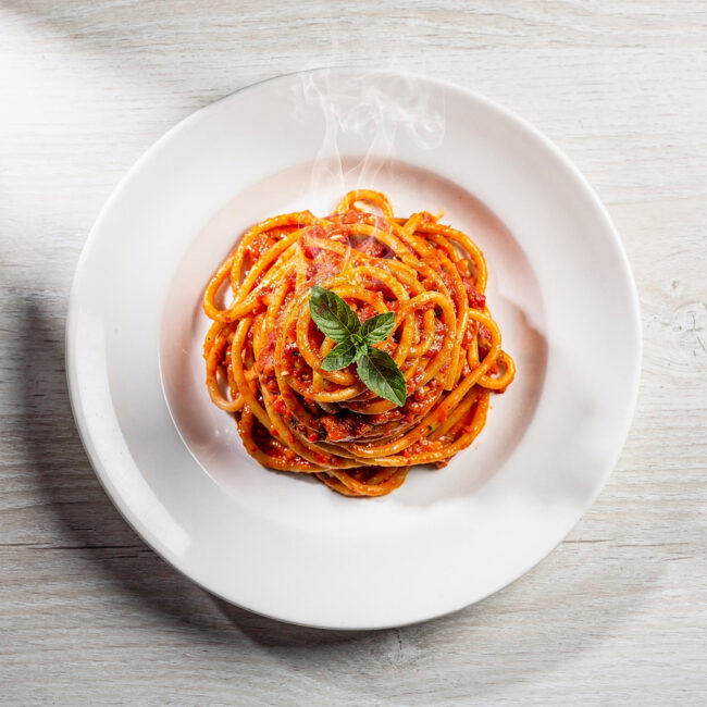 A vibrant bowl of Brazilian pasta topped with fresh herbs and ground peanuts on a rustic wood table.