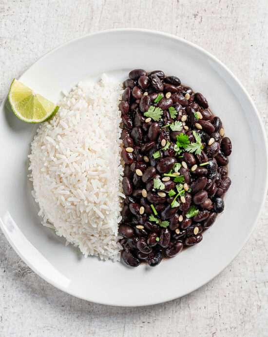 A vibrant, inviting bowl of perfectly cooked brazilian rice and beans, served side-by-side on a rustic wooden table.