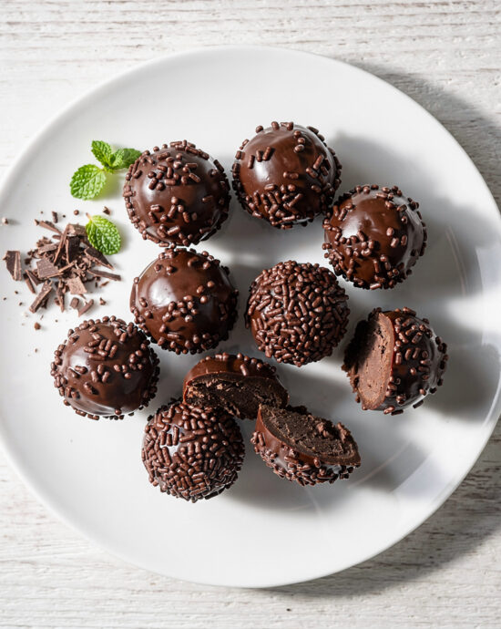 A beautifully styled overhead shot of the finished brigadeiro recipe, featuring glossy chocolate truffles rolled in colorful sprinkles.